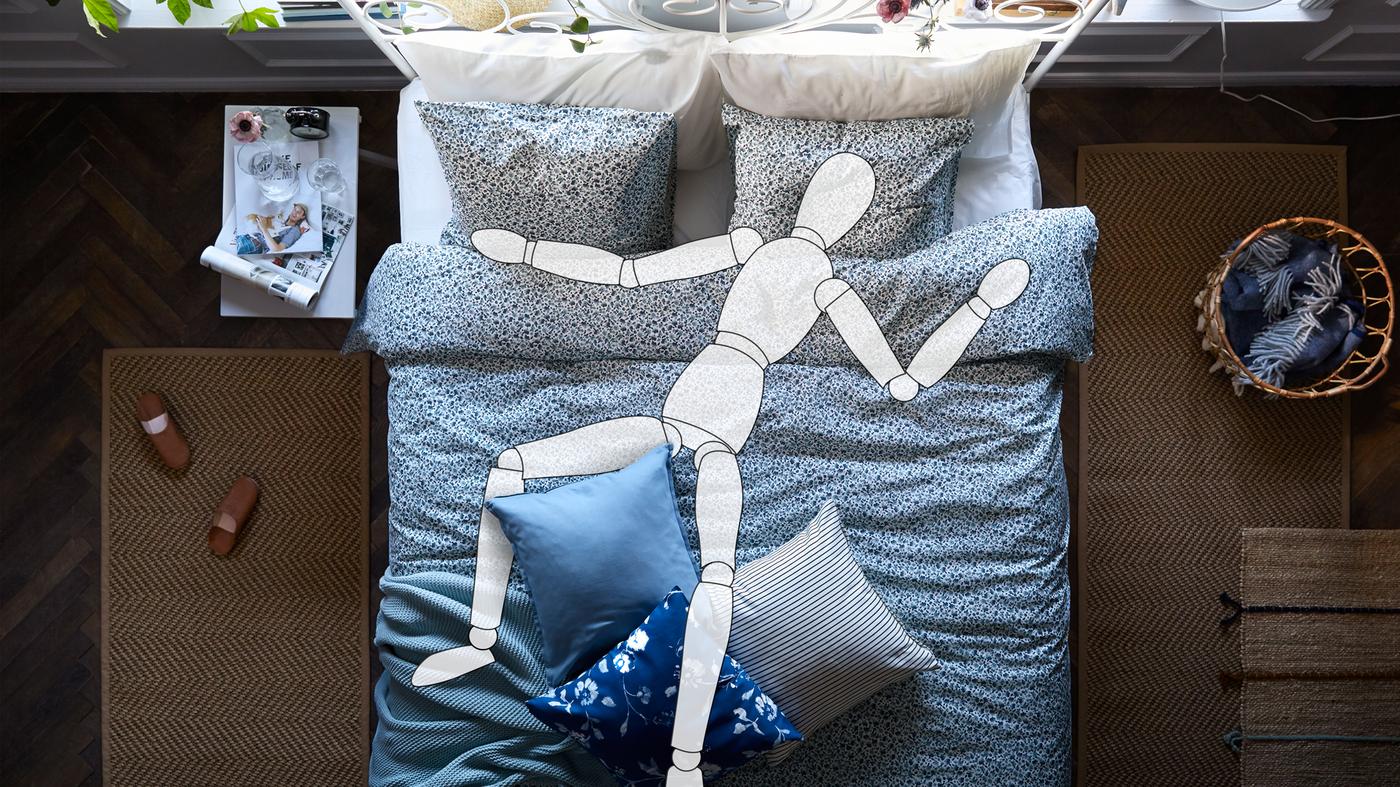 Tegning av ei dukke i ei LEIRVIK seng med VATTENMYNTA sengetøy. På hver side av senga ligger det et brunt gulvteppe.