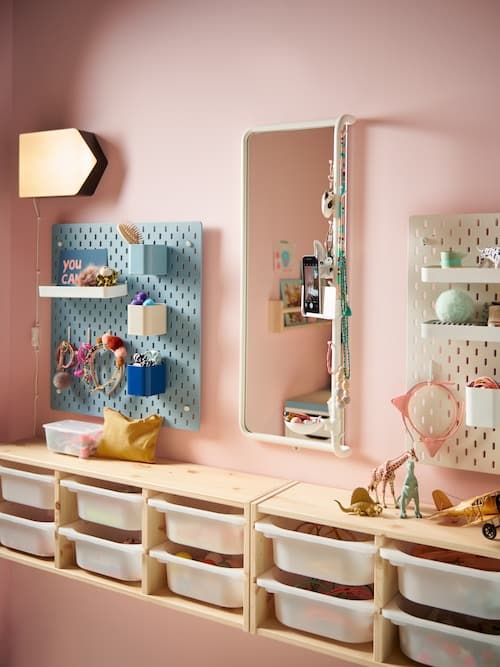 Teil eines Kinderzimmers mit einem hohen Spiegel und Lochplatten an der Wand. Darunter ist eine Vielzahl ausziehbarer Aufbewahrungen zu erkennen.