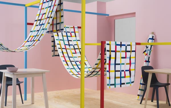 Telas con estampado multicolor colgadas en estructuras coloridas en una habitación rosa.