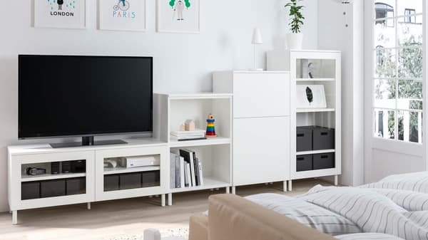 Televize stojí na bílém televizním stolku se skleněnými dvířky. Vedle ní je bílá otevřená police, nízká skříňka a skleněná vitrína.