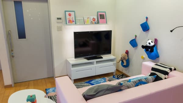 テレビの前にピンクのソファが置かれ、壁にぬいぐるみが飾られている。