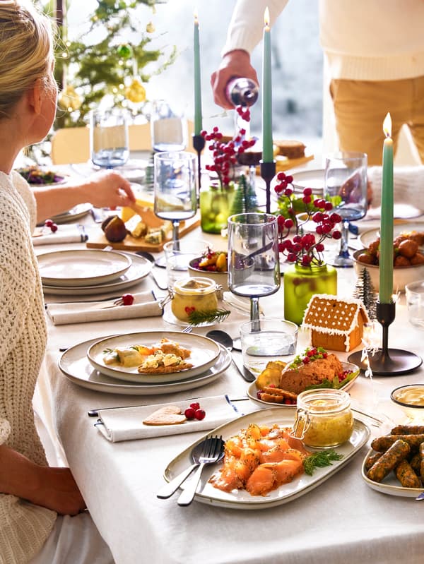 Terített asztal GLADELIG étkészlettel, az asztal közepén fekete FULLTALIG gyertyatartók, amelyekben JUBLA gyertyák égnek.