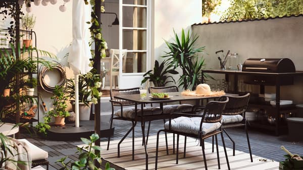Terrasse avec table VIHOLMEN entourée de quatre chaises LÄCKÖ. Contre le mur, cuisine d’extérieur avec barbecue au charbon.