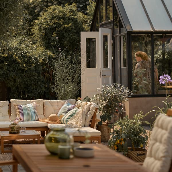 Terrasse mit einem hellbraunen Modulsofa mit beigen Polstern, einem hellbraunen Tisch und einem Hochlehner.