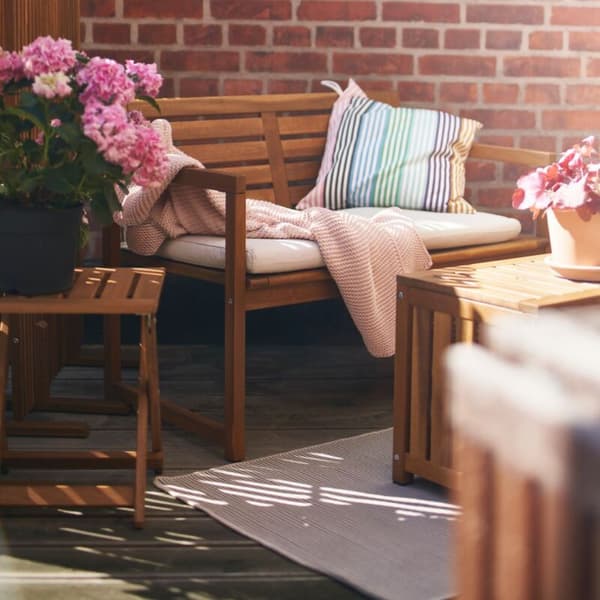 Terraza con conjunto de madera exterior formado por sofá y baúl cerrado que sirve como mesa. El sofá tiene cojines, manta y colchoneta. 