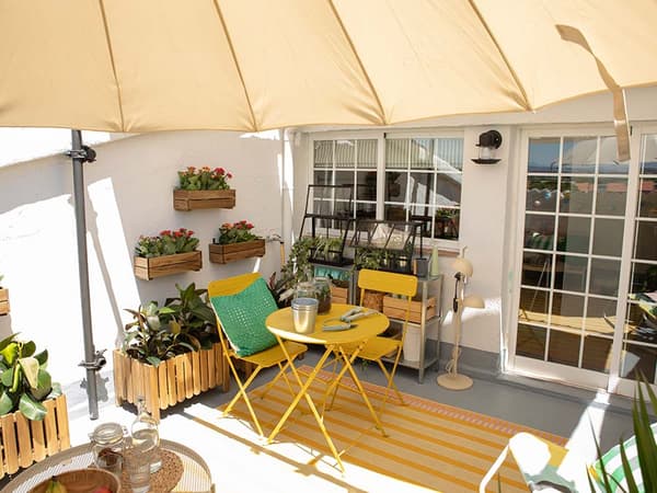 Terraza con sombrilla, conjunto de mesa y sillas, alfombra, macetas de madera con plantas y elementos de jardinería