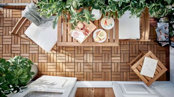 Terraza en plano cenital con conjunto de mesas, silla y mesita de apoyo de madera. Sobre la mesa está puesto el desayuno. Hay plantas y el suelo está formado de módulos  de madera.