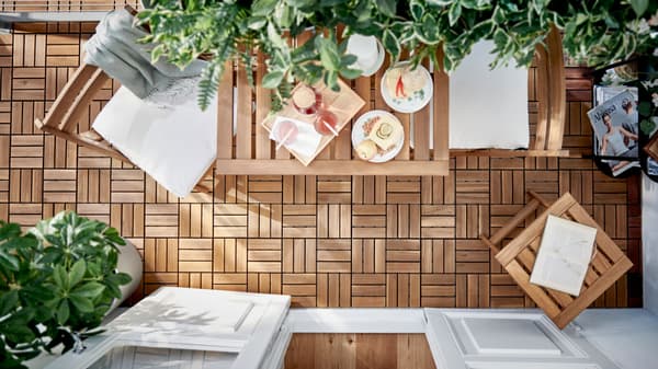 Terraza en plano cenital con conjunto de mesas, silla y mesita de apoyo de madera. Sobre la mesa está puesto el desayuno. Hay plantas y el suelo está formado de módulos  de madera.