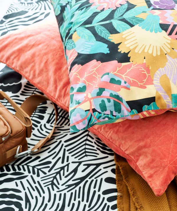 Țesătură cu model în alb și negru cu o pernă din catifea culoarea somonului și o pernă cu model multicolor.