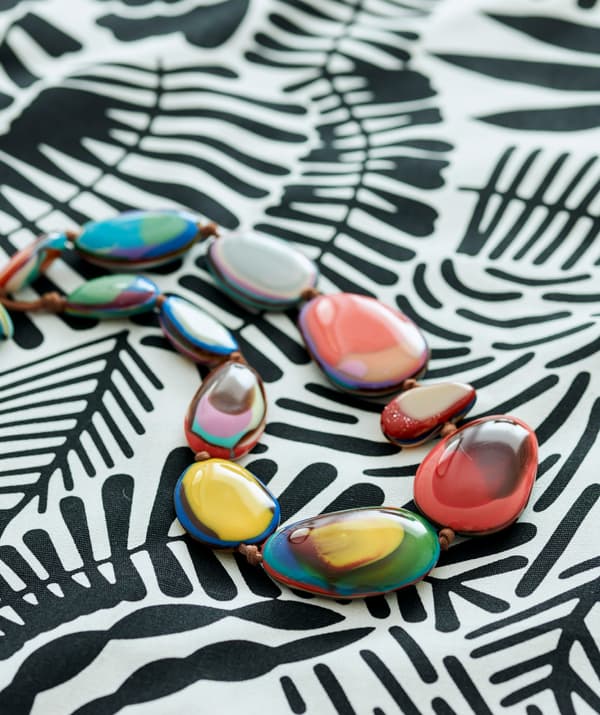 Țesătură cu model în alb și negru pe care este așezat un colier din mărgele sferice în diferite culori.