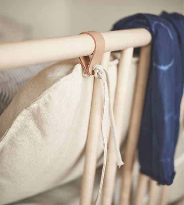 Testiera del letto in legno BJÖRKSNÄS con laccio in pelle e biancheria in lino bianca. Sulla testiera è appoggiato un vestito di colore blu.