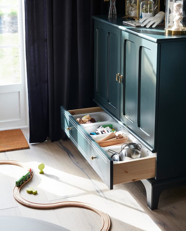 The bottom drawer of a LOMMARP cabinet is open. Children’s toys are stored inside, and there’s a train set on the floor.