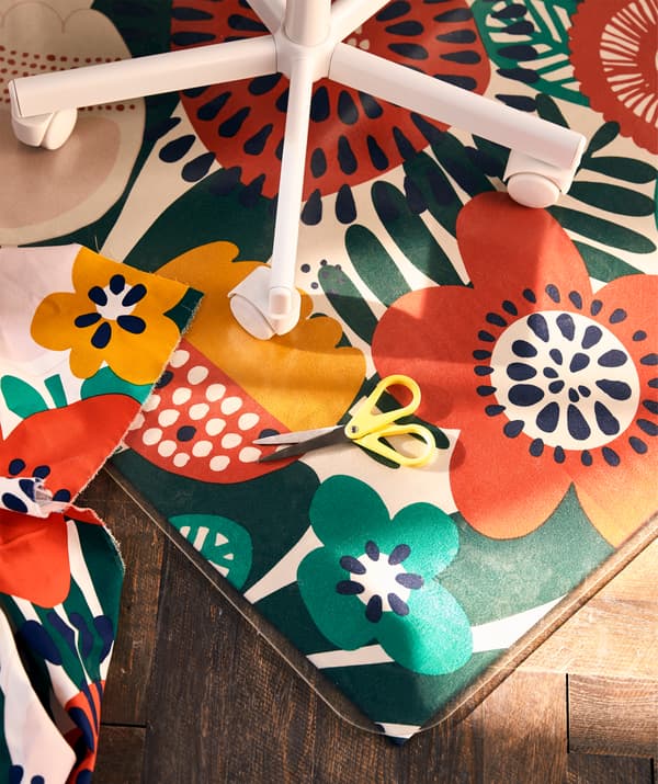 The bottom part of a children’s swivel chair standing on a floor protector, a length of flower-pattern fabric underneath.