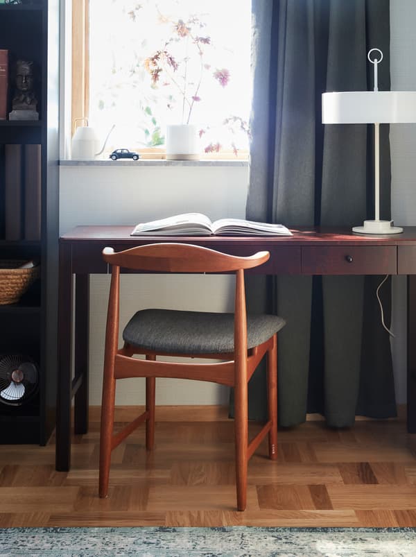 The chair DANSKE in oak with a textile seat designed for IKEA in the 60’s, standing in front of a desk in dark wood.
