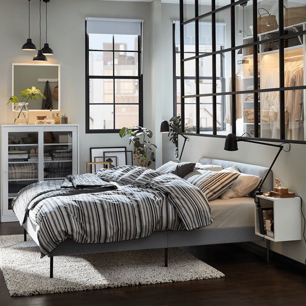 The curved corner of a blue TUFJORD bed, in front of a wooden wall with built-in bookshelf and next to a bedside table.