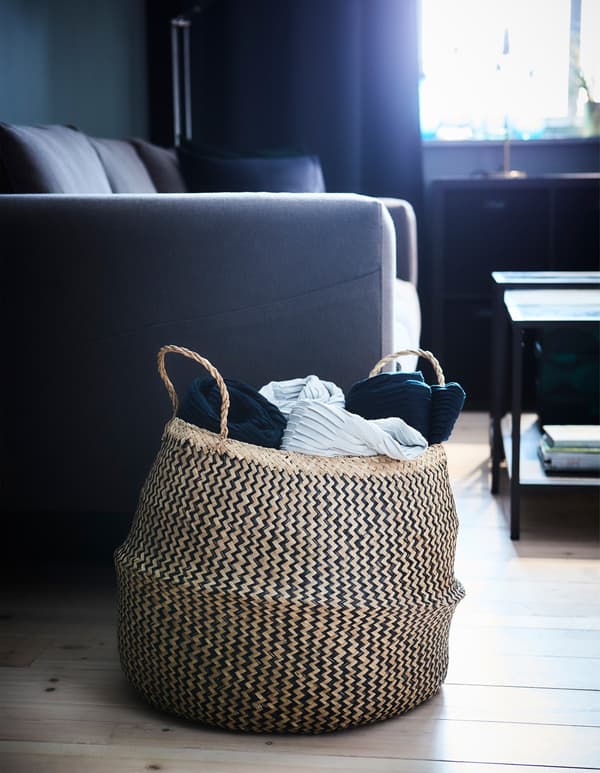 The decorative FLÅDIS basket made of natural woven material stores throws and other textiles in a living room.