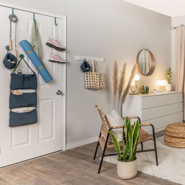 The door of a bedroom is used to store workout equipment such as jump rope, yoga mat, and running shoes. Inside the bedrom is a chair, footstool, plant, and a dresser.