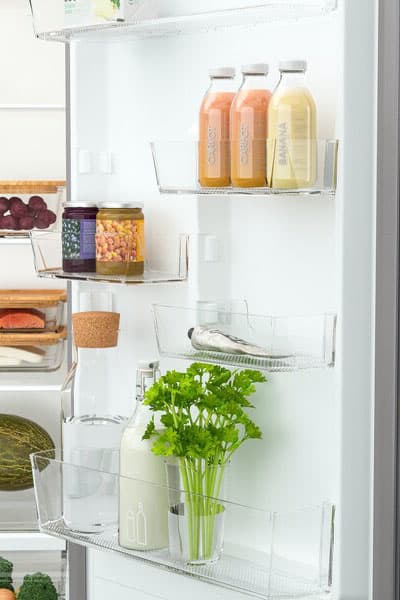 The door of a fridge open showing the different shelves filled with juice, jams and fresh. herbs.
