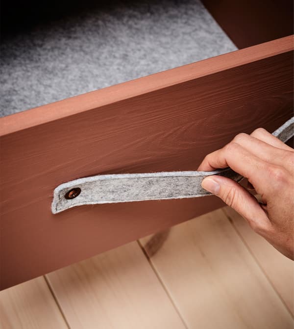 The drawer of a bedside table is lined with grey felt and has a felt handle.