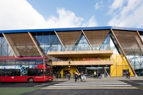The entrance of an IKEA store from the outside, with a red double decker bus stopping to let people cross the street and enter the IKEA store.