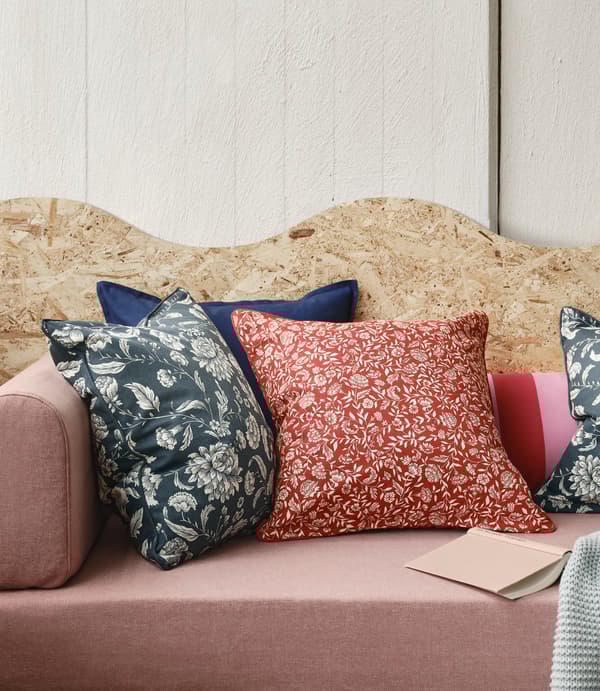 The floral EVALOUISE and IDALINNEA cushion covers are placed in a pink sofa with a plywood structure behind.