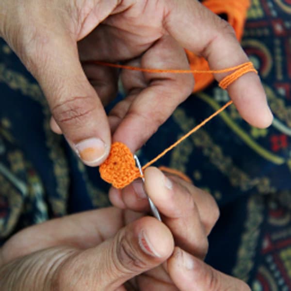 The hands of an artisan crocheting using orange yarn.
