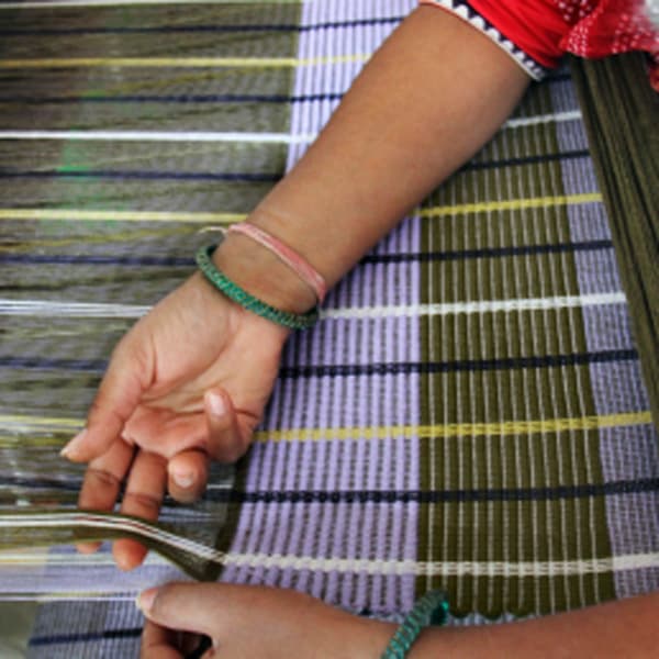 The hands of an artisan weaving a MÄVINN rug.