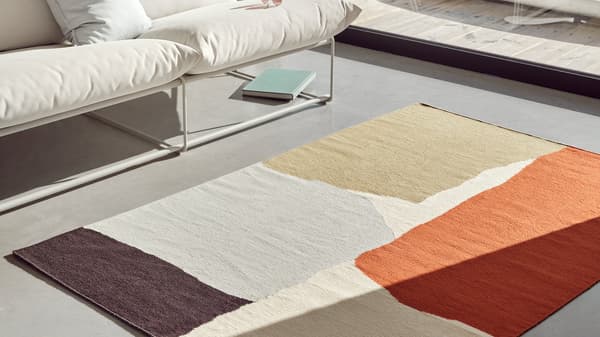 The handwoven TVINGSTRUP rug is placed on gray screed flooring in a modern living room.
