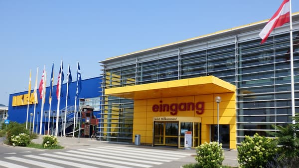 The image shows the entrance area of an IKEA store with a glass facade, a yellow canopy, and the word 