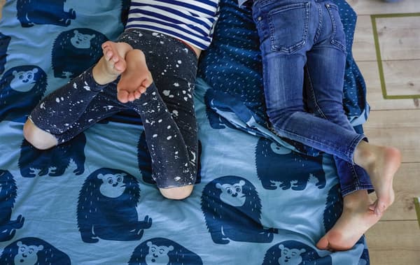 The legs of two boys laying on a bed with blue animal-patterned bedding.