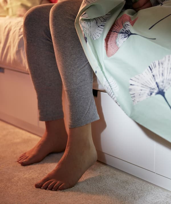 The lower part of a white bed, with built-in storage boxes, with two feet landing on a plush rug.