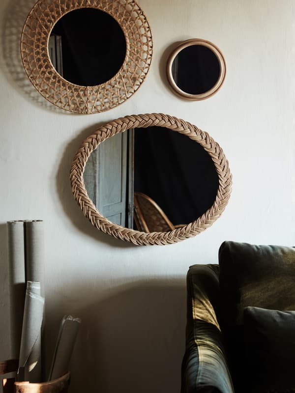 The oval KRISTINELUND mirror made in decoratively woven rattan, hanging on a grey wall with other woven mirrors.