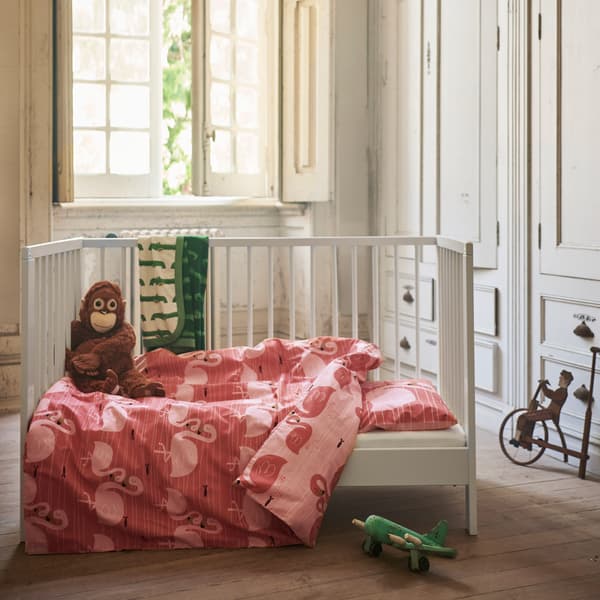 The pink two-sided RÖRANDE quilt cover and pillowcase with a print of cuddling flamingos placed in a child’s bed.