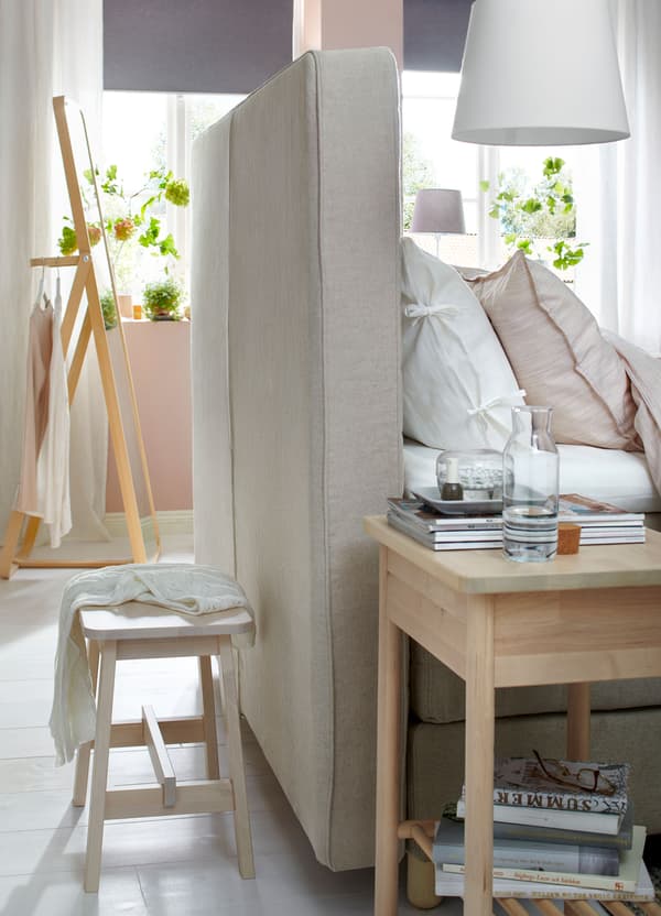 The rear view of the fabric headboard of an IKEA HOMMELVIK beige divan bed next to a bedside table.
