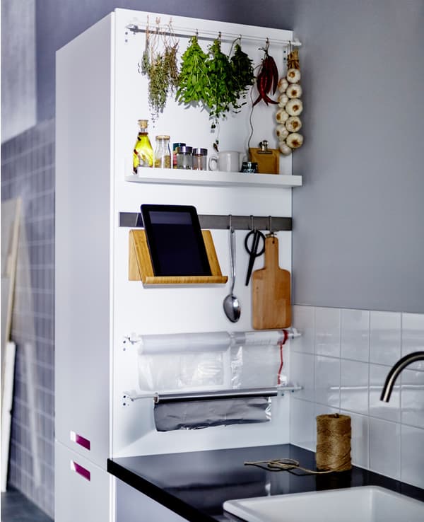 The side of a kitchen cabinet next to a countertop on which spices, scissors and a tablet stand are stored and organised.
