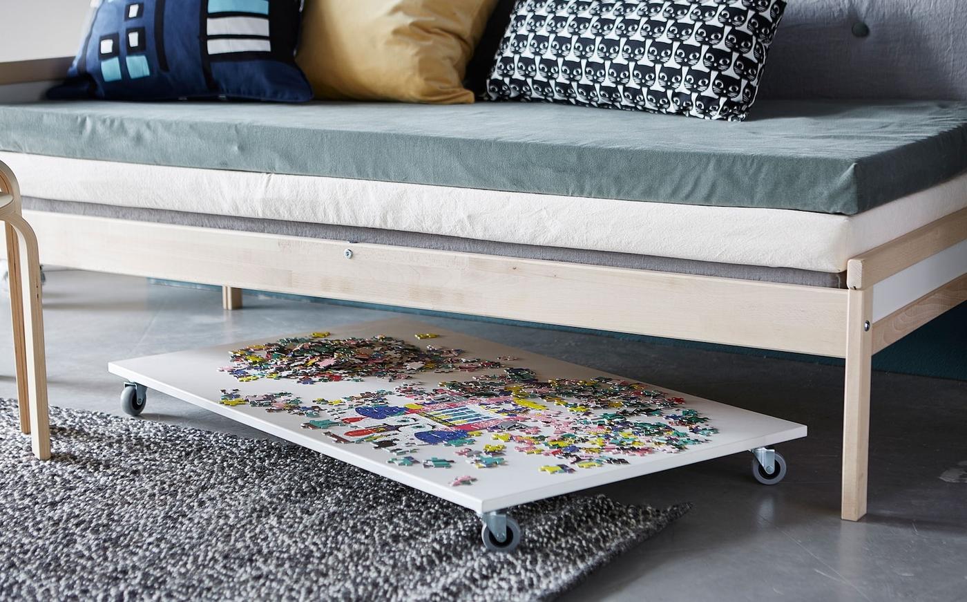 The side view of a puzzle board on wheels under a sofa.