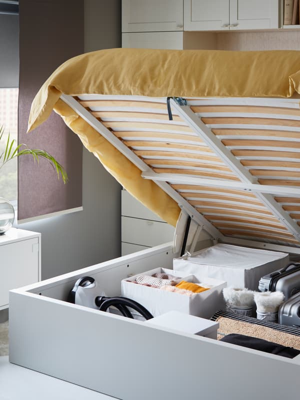 The storage space under a white IKEA MALM ottoman bed is revealed and holds extra quilts, pillows and seasonal clothing.