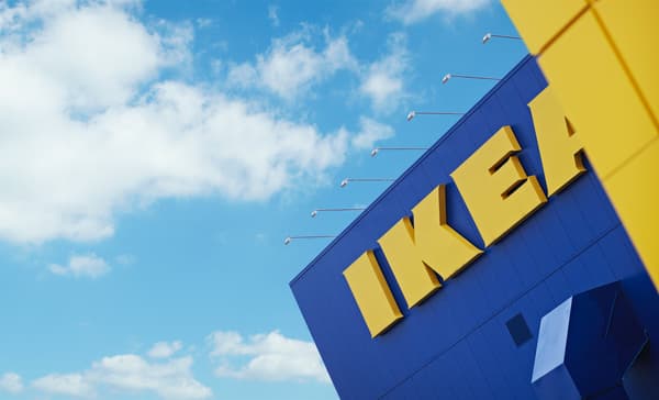 The sun is shining through the glass shopfront of an inner-city IKEA store. The entrance is framed in bright yellow.