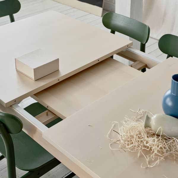 The table leaf extension lying under the table top of RÖNNINGE extendable table in light birch placed in a dining context.