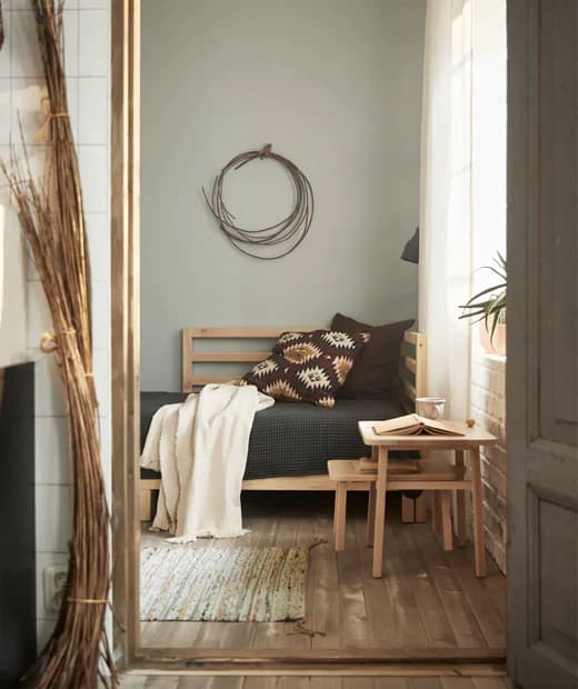 The TARVA day bed with neutral textiles, a natural wood side table and a small carpet on hardwood floors in a multi purpose room.