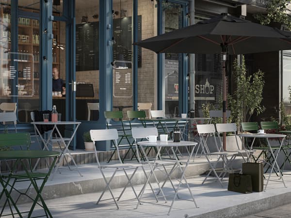 The terrace of a café with grey and green SUNDSÖ chairs and tables in lines facing outwards. An open parasol is on one side.