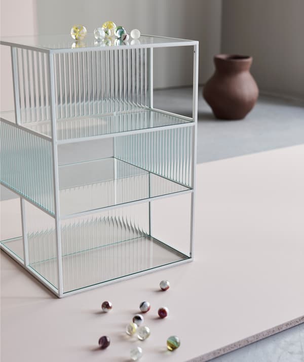 The thin lines and glass panes of a SAMMANHANG display box make a stage for whatever you place in, on or beside it. Here visualised by a handful of glass beads and an INDUSTRIELL vase.