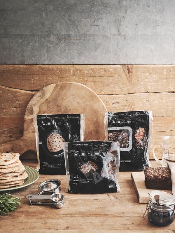 The three KNÅDA bread baking mixes in their packaging are standing on a wooden kitchen counter.