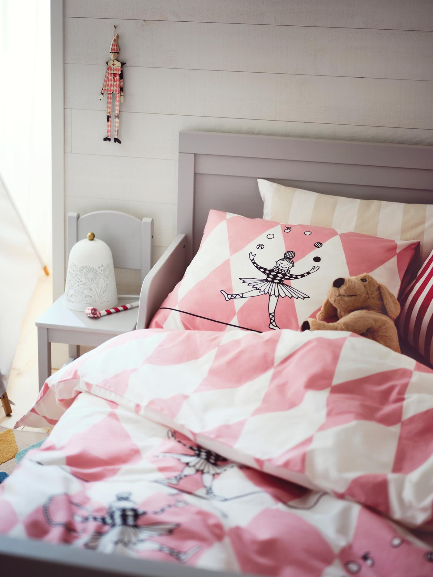 The top end of a grey SUNDVIK extendable bed covered with pink and white BUSENKEL bed linen with a soft toy in the bed.