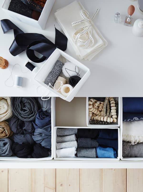 The top of a chest of drawers covered with sewing accessories. An open drawer reveals garments neatly placed in SKUBB boxes.