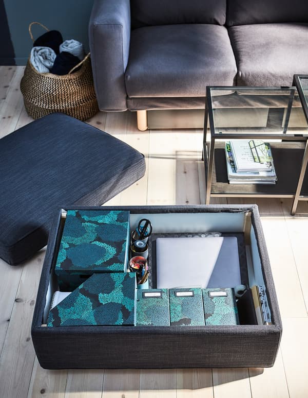 The top of a footstool is removed to reveal a storage space filled with small organisation boxes.