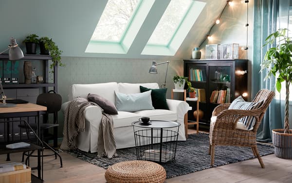 The traditional EKTORP 2-seat sofa in Vittaryd white sits opposite a BYHOLMA/MARIEBERG wicker chair in a small, cosy green, grey and white sitting room with a sloping roof.