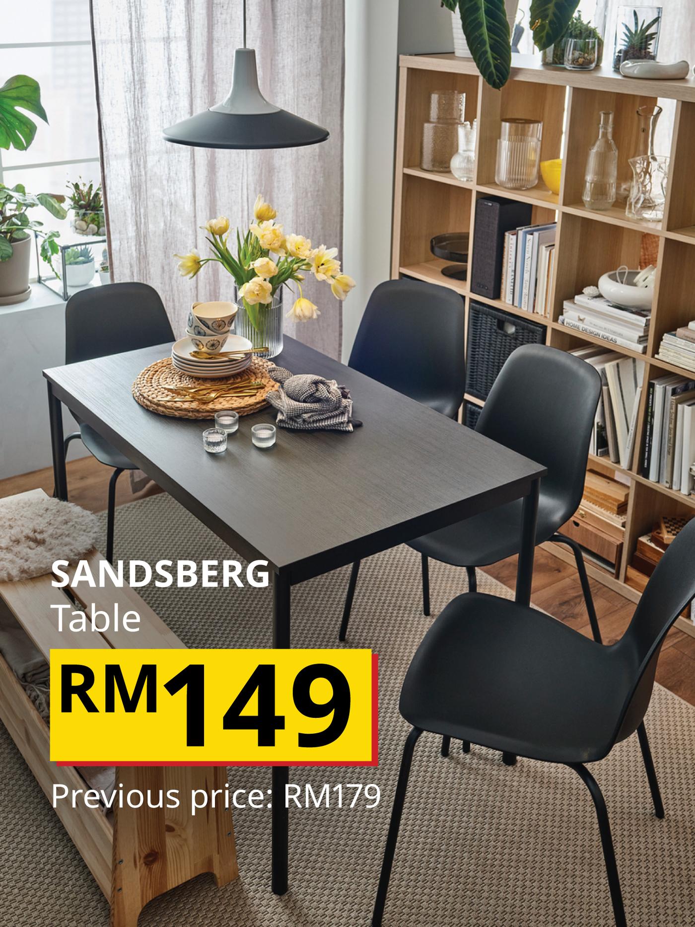 The visual shows a SANDSBERG dining table surrounded by black dining chairs in a bright dining area with shelving and plants. The text reads: “SANDSBERG Table, RM149. Previous price: RM179.”