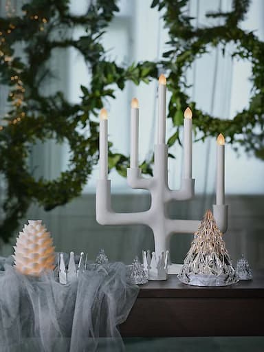 The white IKEA STRÅLA candelabra on a table in front of festive wreaths.