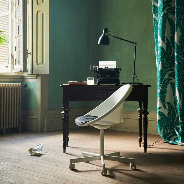 The white LOBERGET/BLYSKÄR swivel chair with a rounded design placed by an old desk near an open window in a green room.